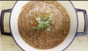 Hearty homemade Bolognese sauce with fresh herbs in a large pot on a wooden board.